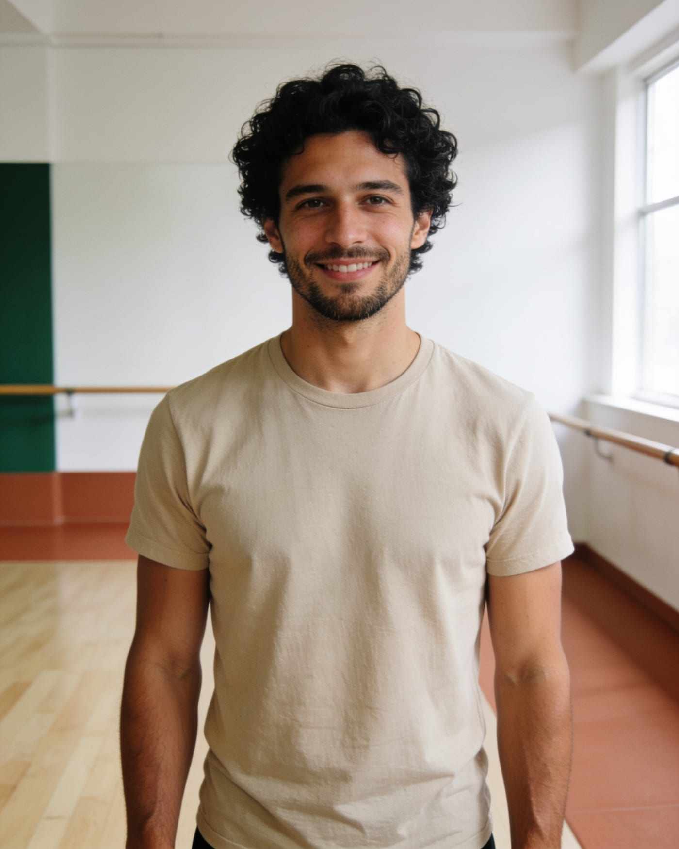 Devon, with curly black hair and an oatmeal tee, smiling in the studio.