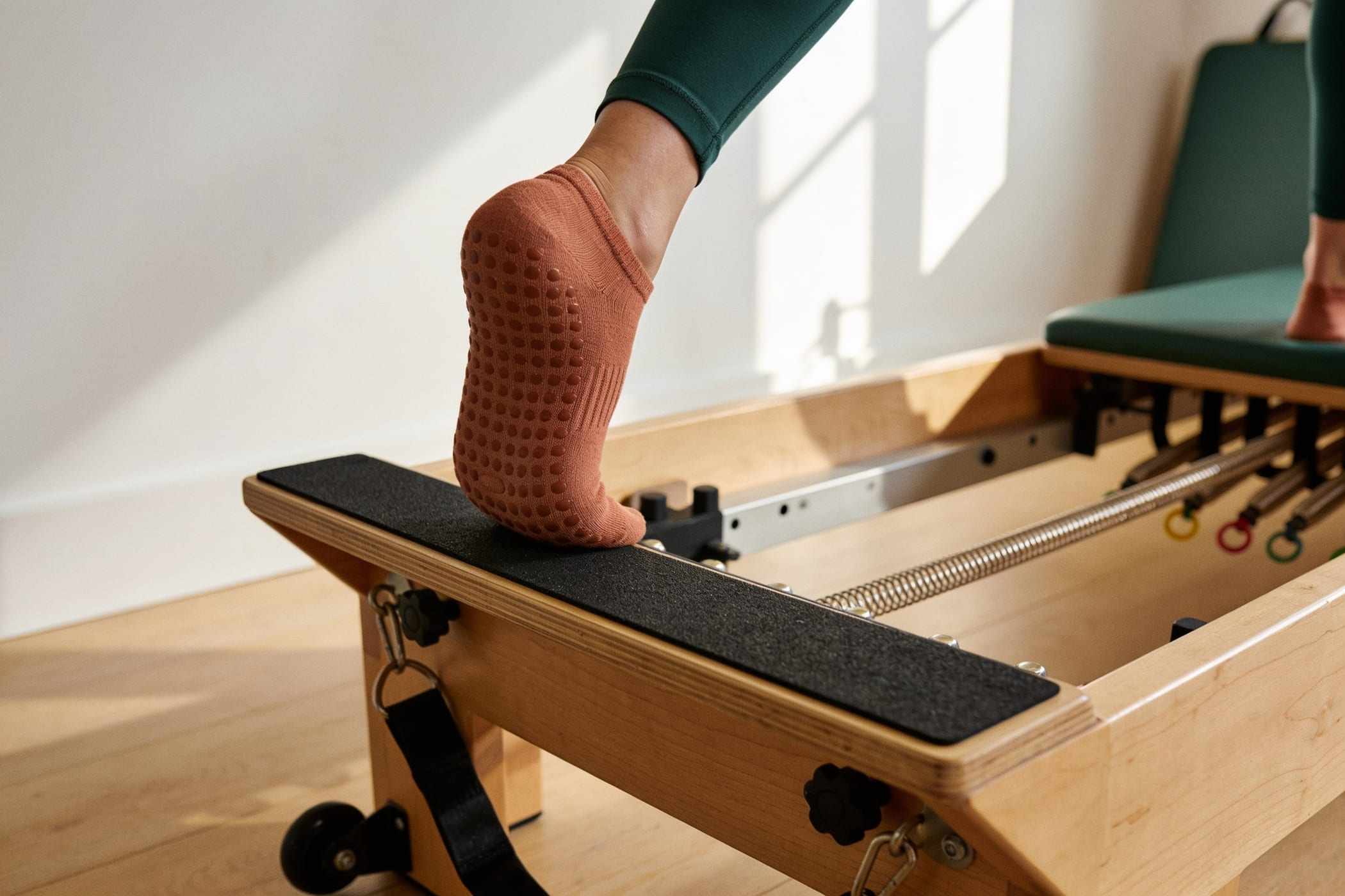 Feet in grip socks resting on the footbar of an oak reformer.