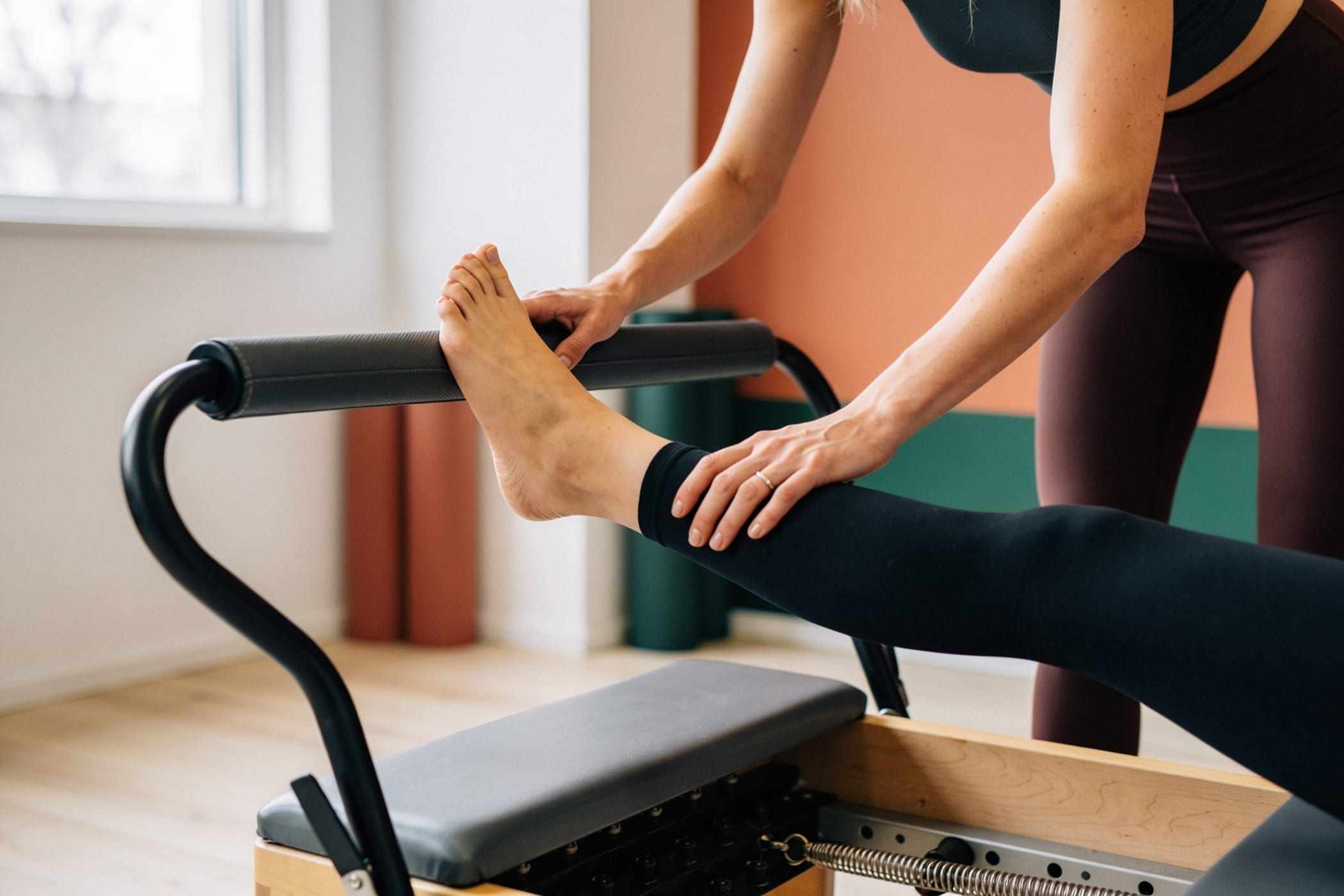 An instructor guides a client’s foot on the reformer footbar.