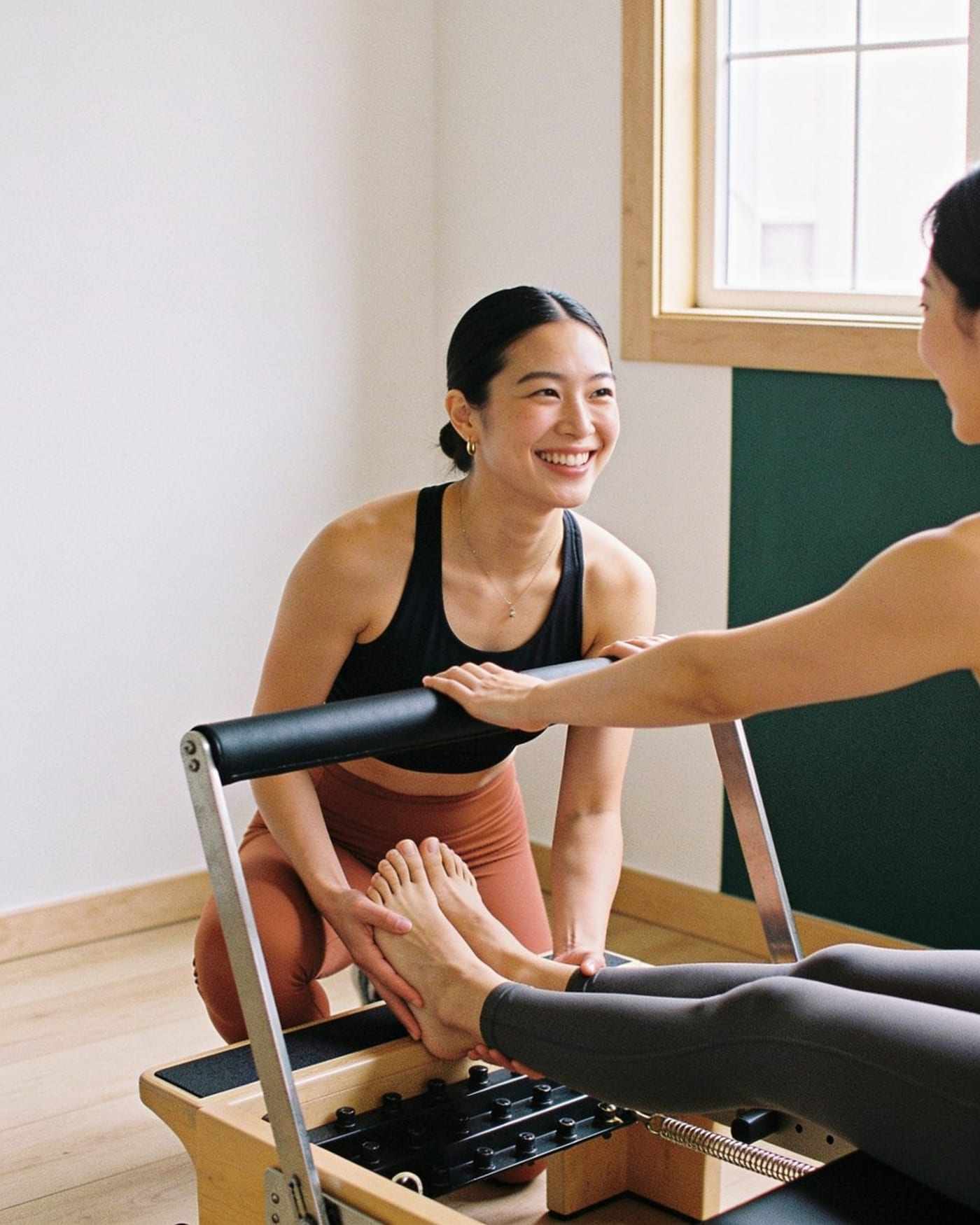 An instructor adjusts a beginner’s foot on the reformer bar.