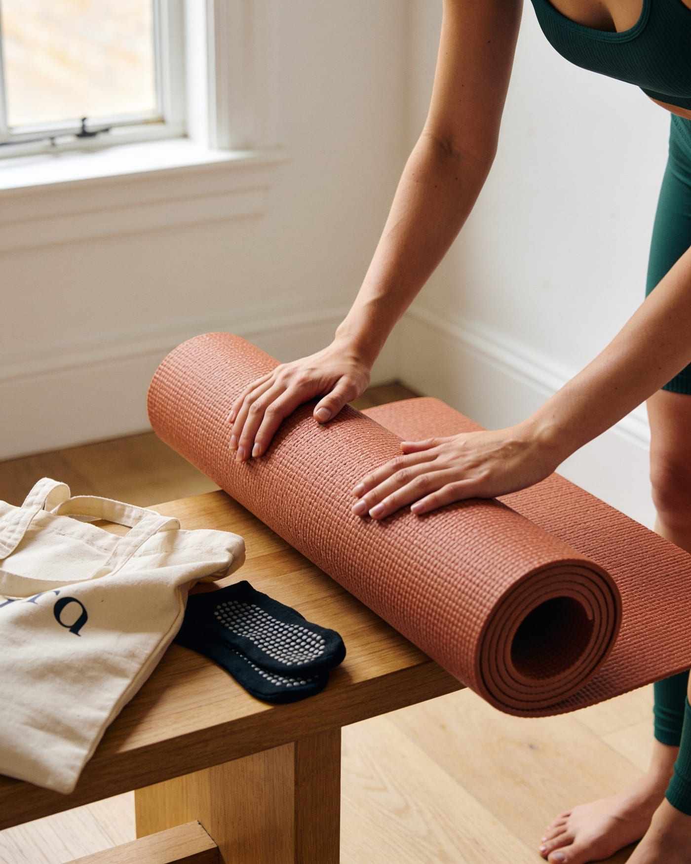A woman rolls up her mat after class beside her bag and grip socks.
