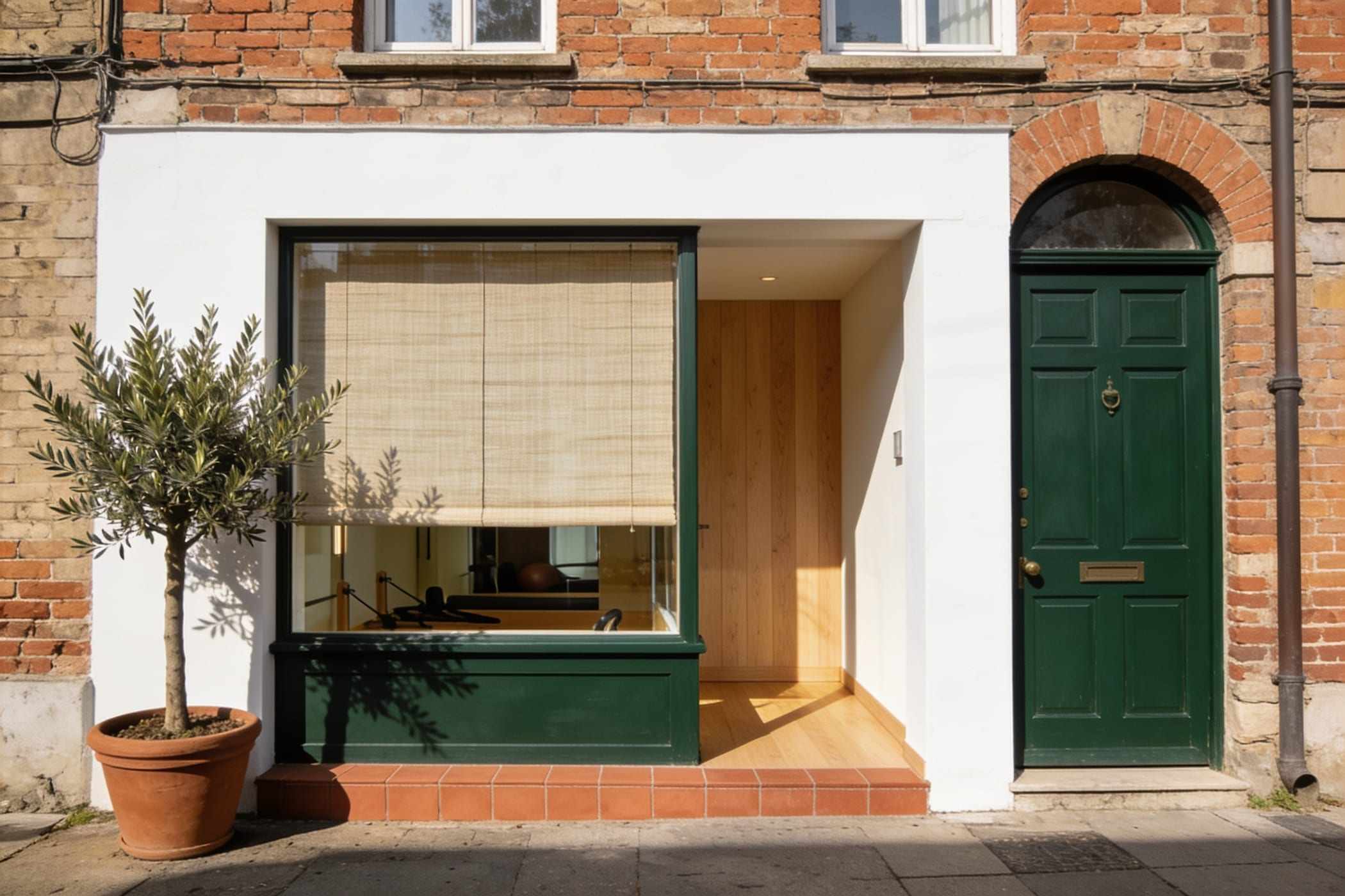 The studio front: a green door and a large window with linen blinds in an old brick building.